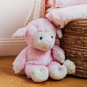 Cute pink plush lamb toy cozy beside a wicker basket and soft blankets indoors.